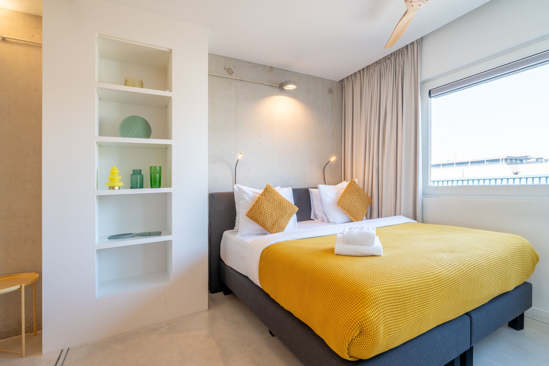 Een moderne slaapkamer met een bed voorzien van een felgele sprei en twee sierkussens, naast een ingebouwde boekenkast.