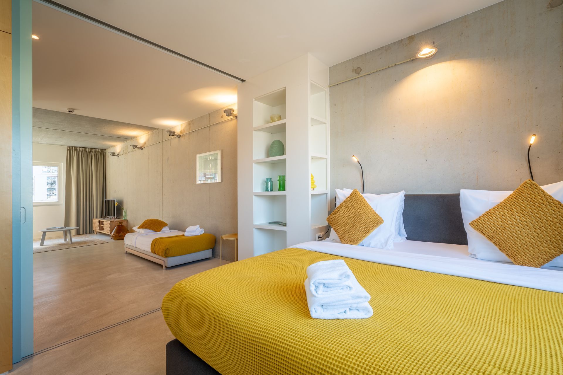 Een hotelkamer met een groot bed op de voorgrond en een tweede bed en zithoek zichtbaar op de achtergrond.