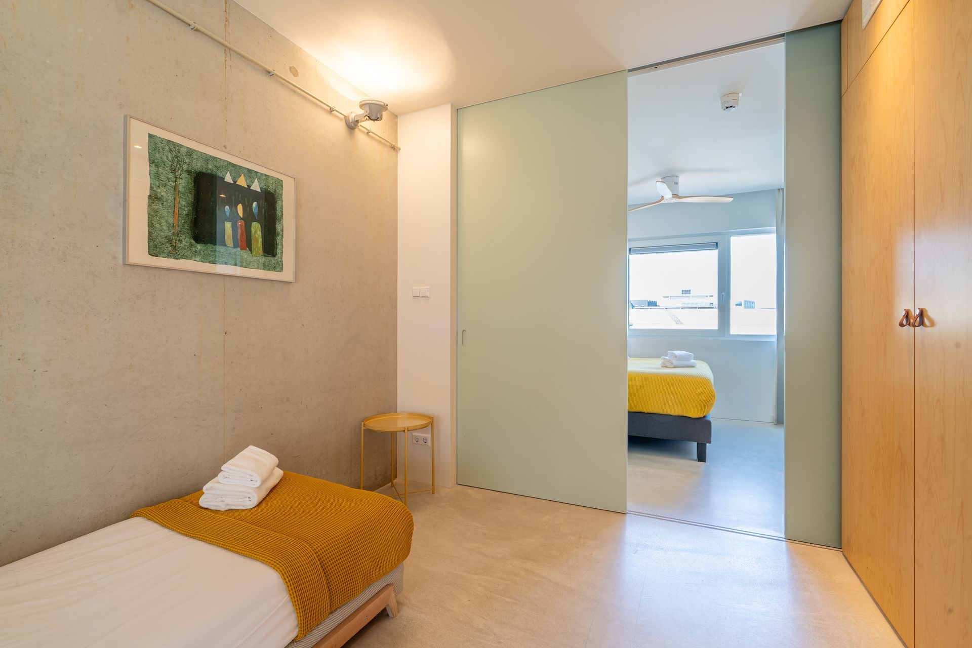 Een moderne kamer met een eenpersoonsbed  schuifdeuren die toegang geven tot een andere slaapkamer.