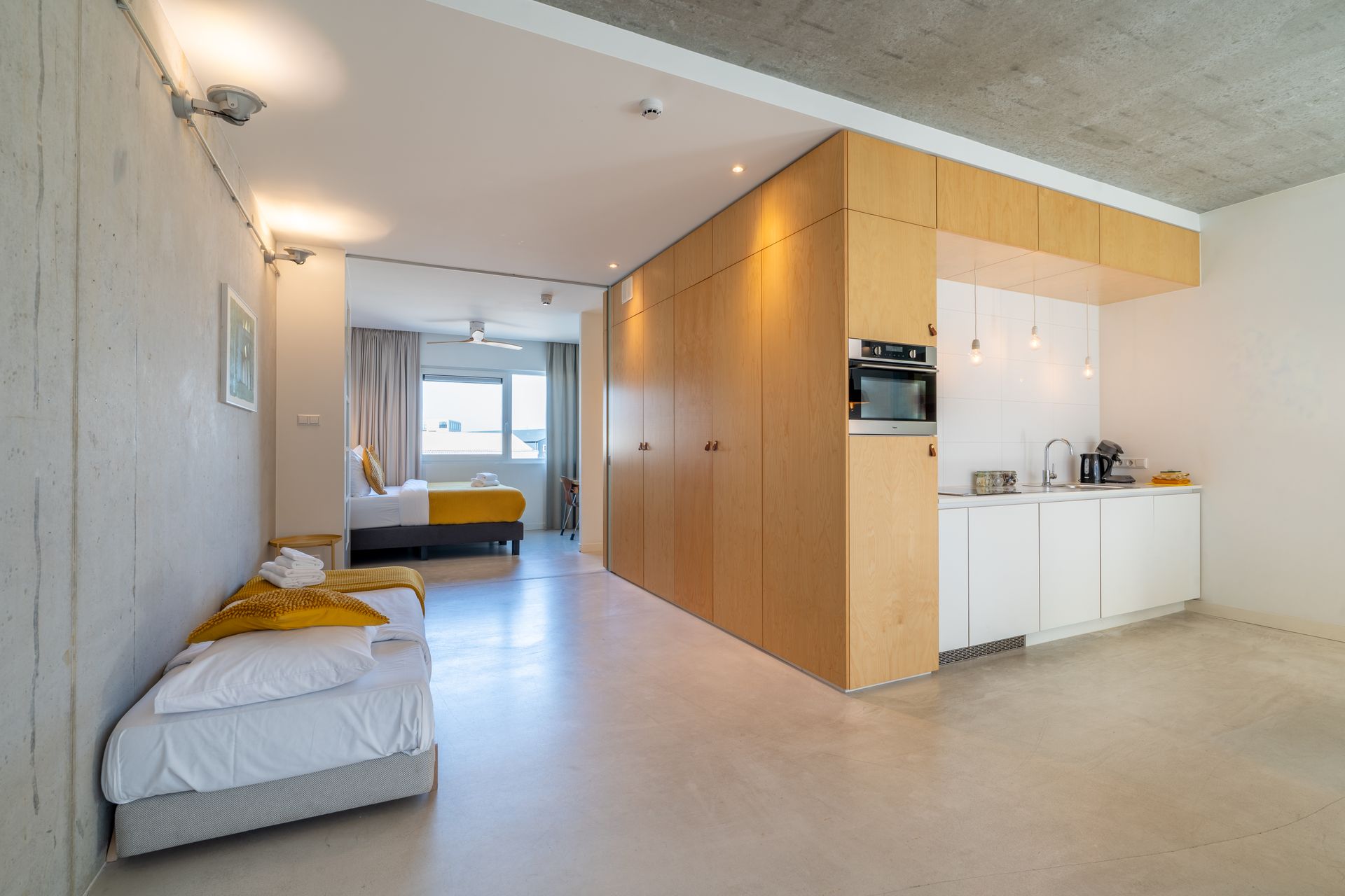Een modern appartement met een keuken, een woonkamer met een bed en een aparte slaapkamer met een bed op de achtergrond.