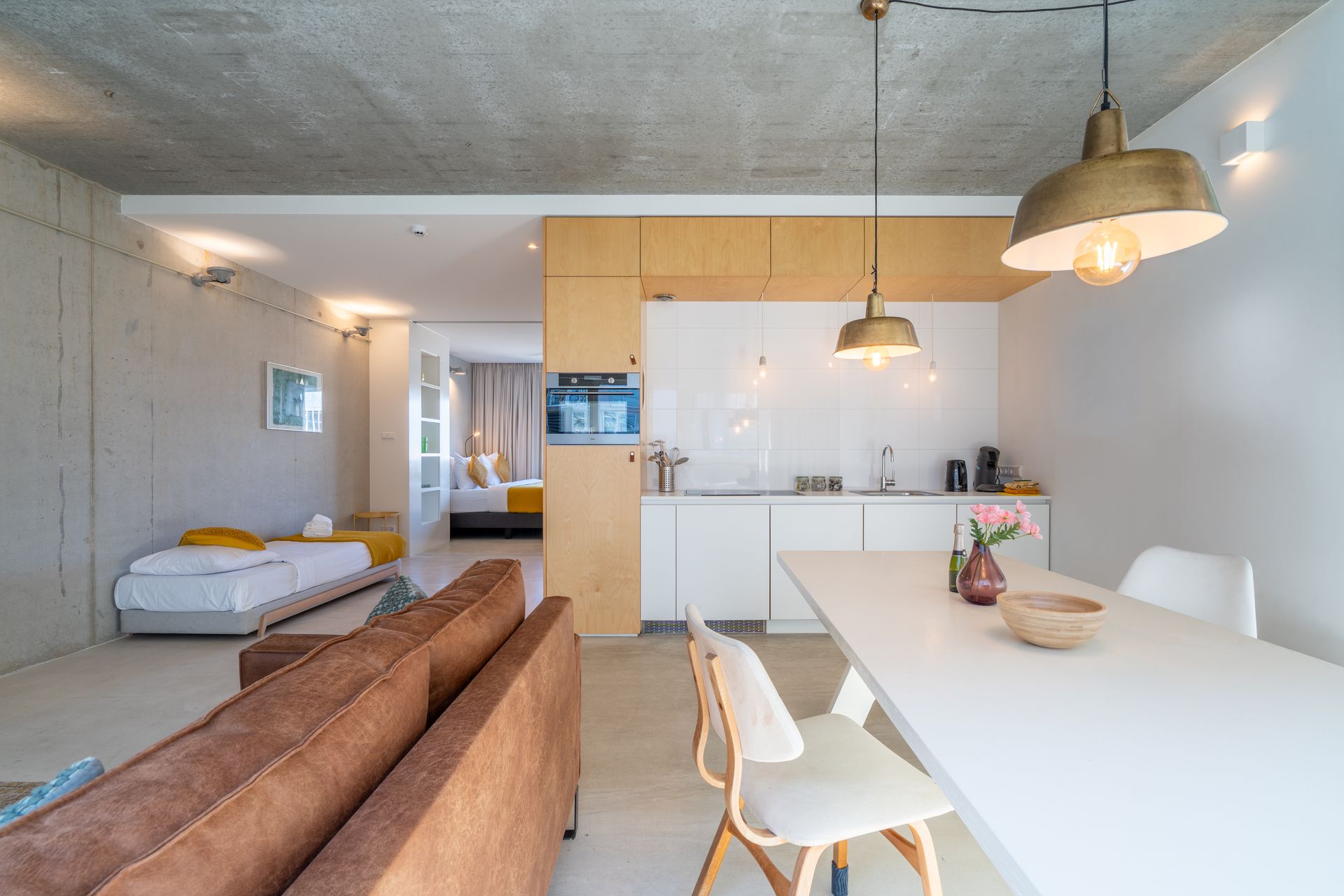 Open woonruimte met een bank, vloerkleed, eettafel en ramen. Witte muren en plafond.