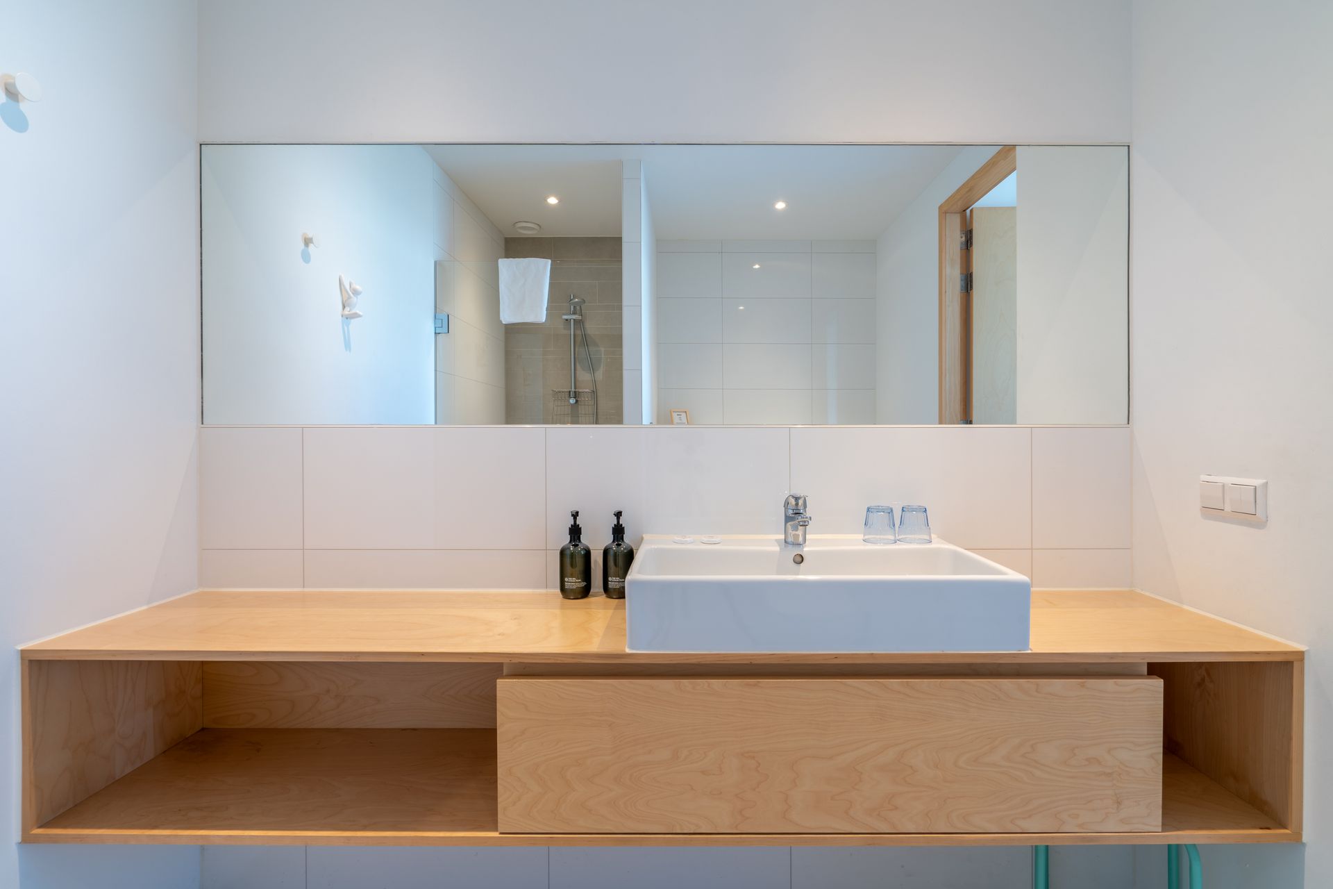 Een moderne badkamermeubel met een witte rechthoekige wastafel op een licht houten blad en een grote wandspiegel.