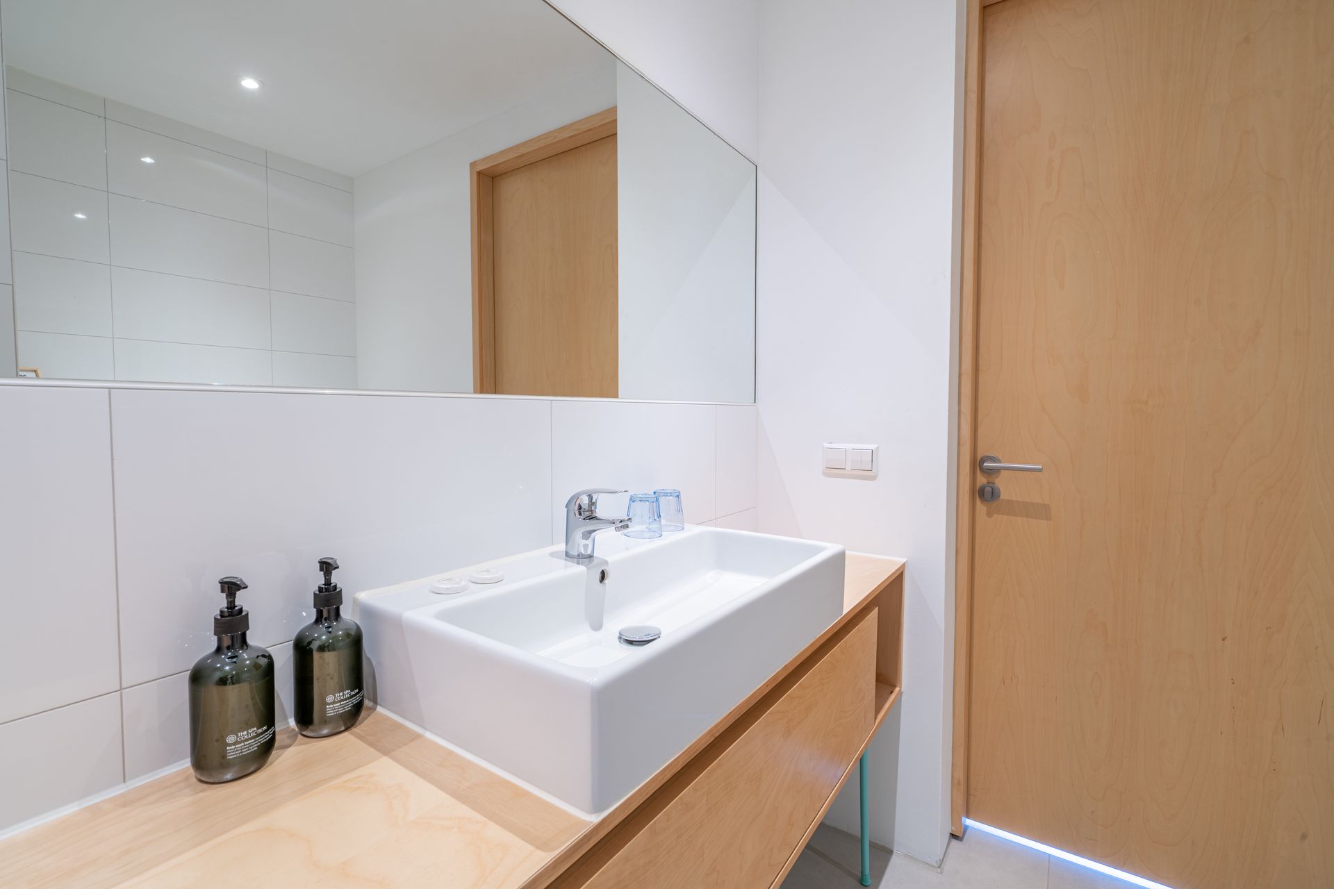 Een minimalistisch badkamermeubel met een witte opbouwspoelbak, een houten blad, een grote spiegel.