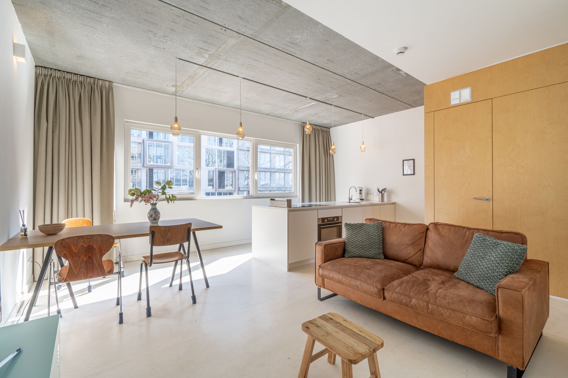 Moderne woonkamer met een bruine bank, een witte eettafel en een ingebouwde keuken.