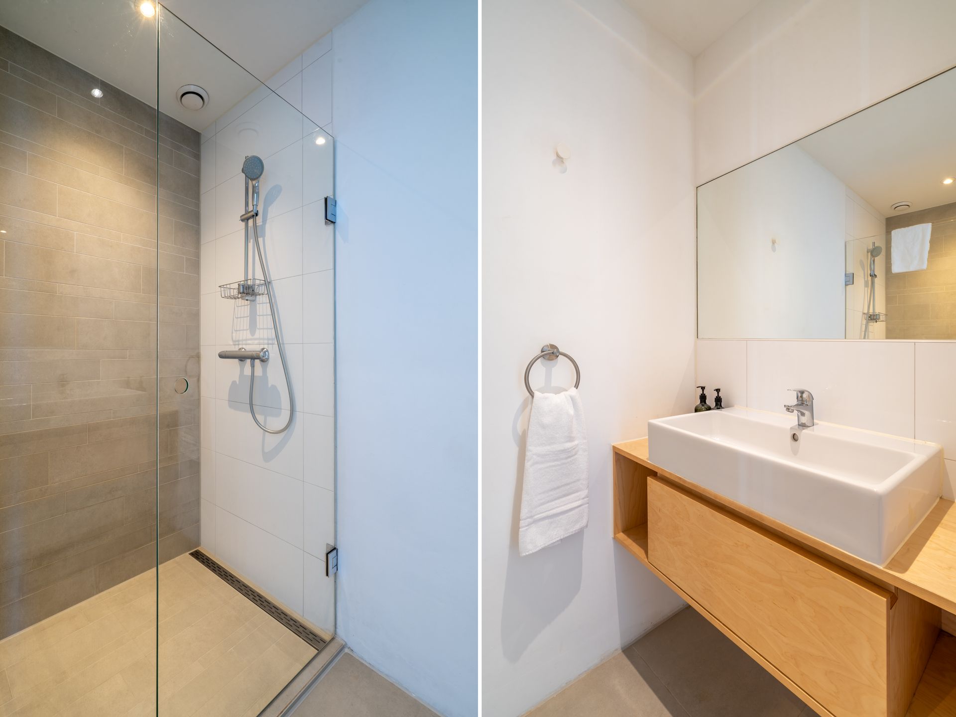 moderne badkamer: een glazen douchecabine met grijze tegels en een houten badmeubel met wastafel.