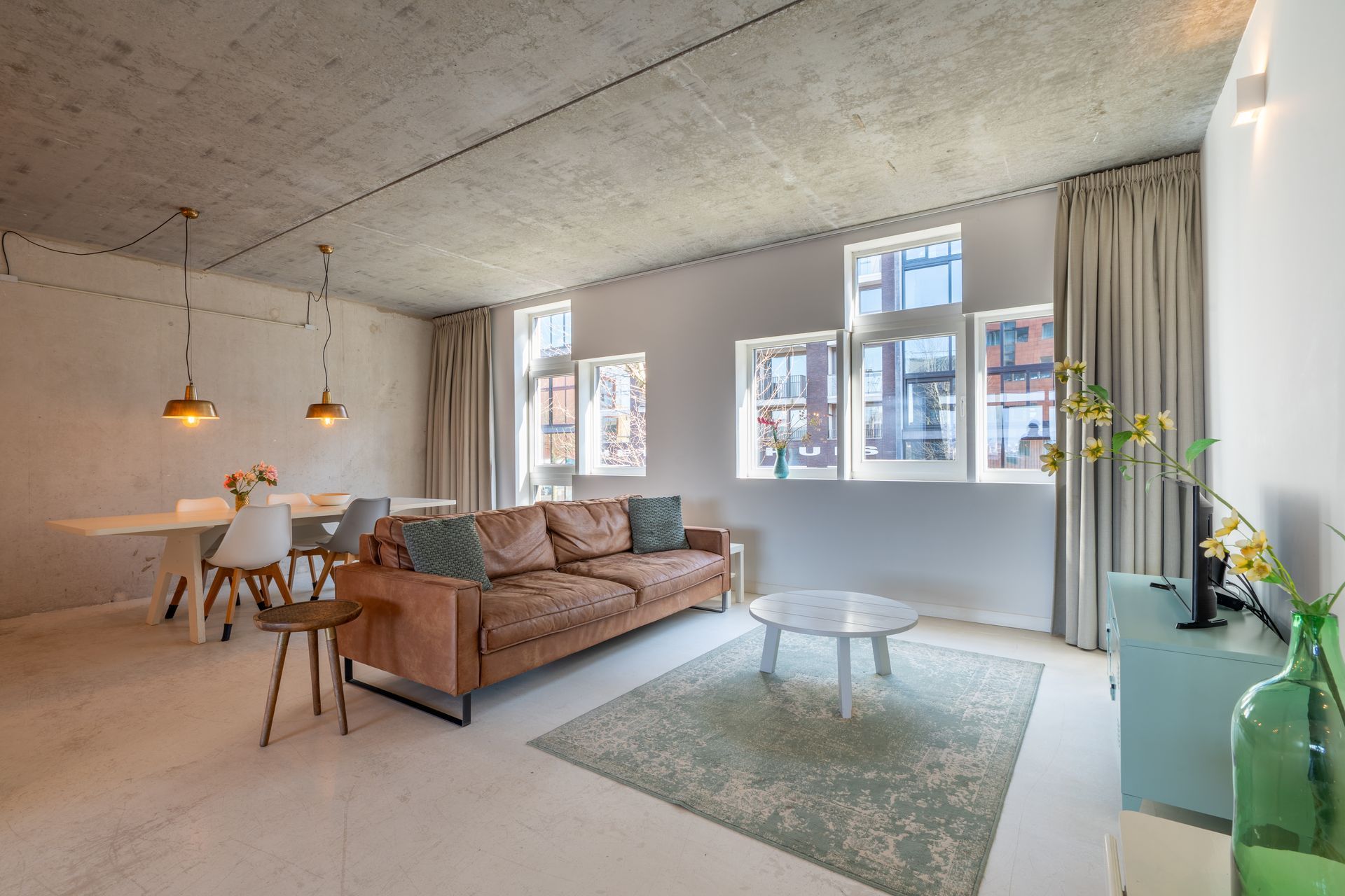 Moderne woonkamer met leren bank, eethoek en witte muren.