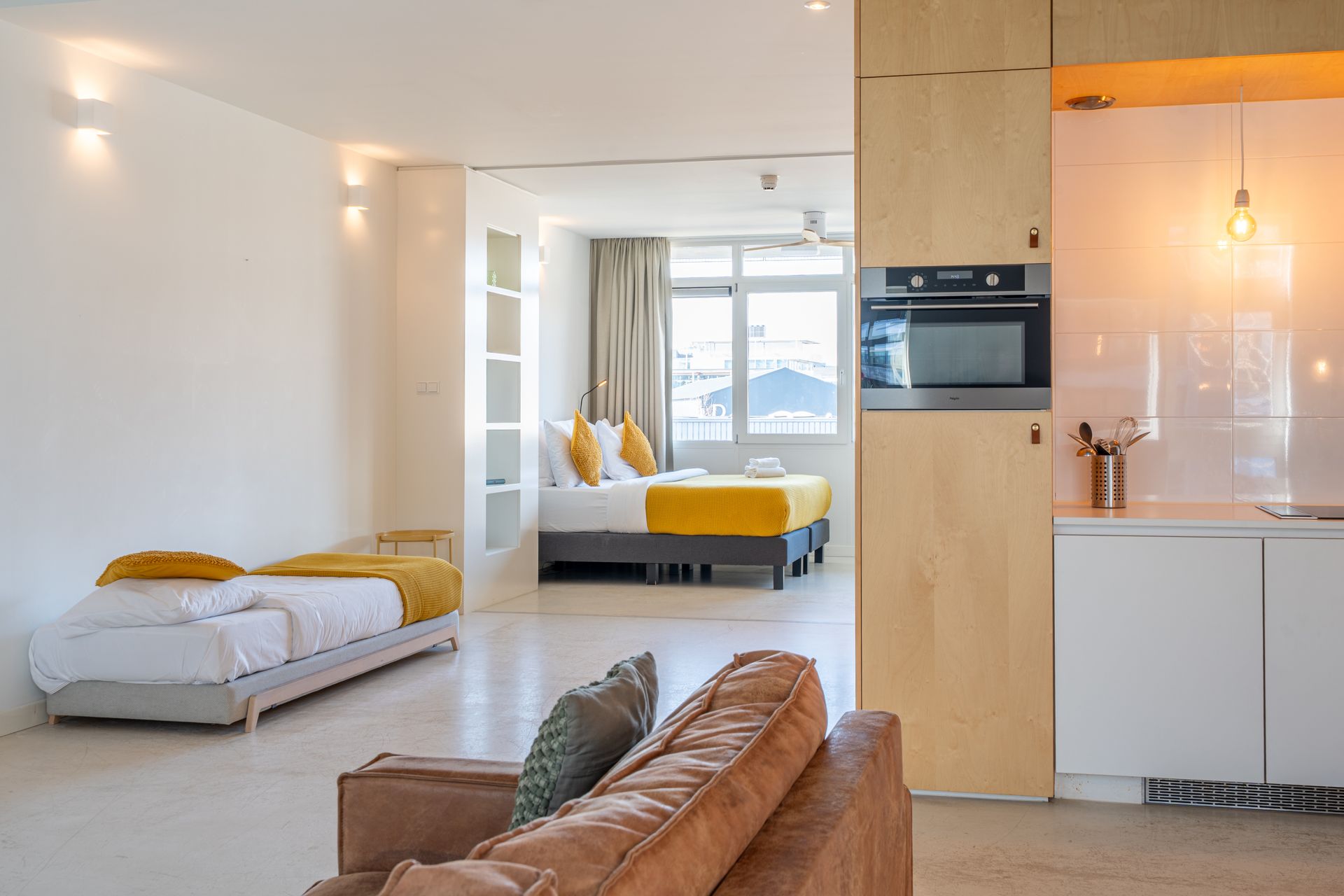 Modern appartementinterieur met een chaise longue, een bank, een keukenhoek en een aparte slaapkamer op de achtergrond.