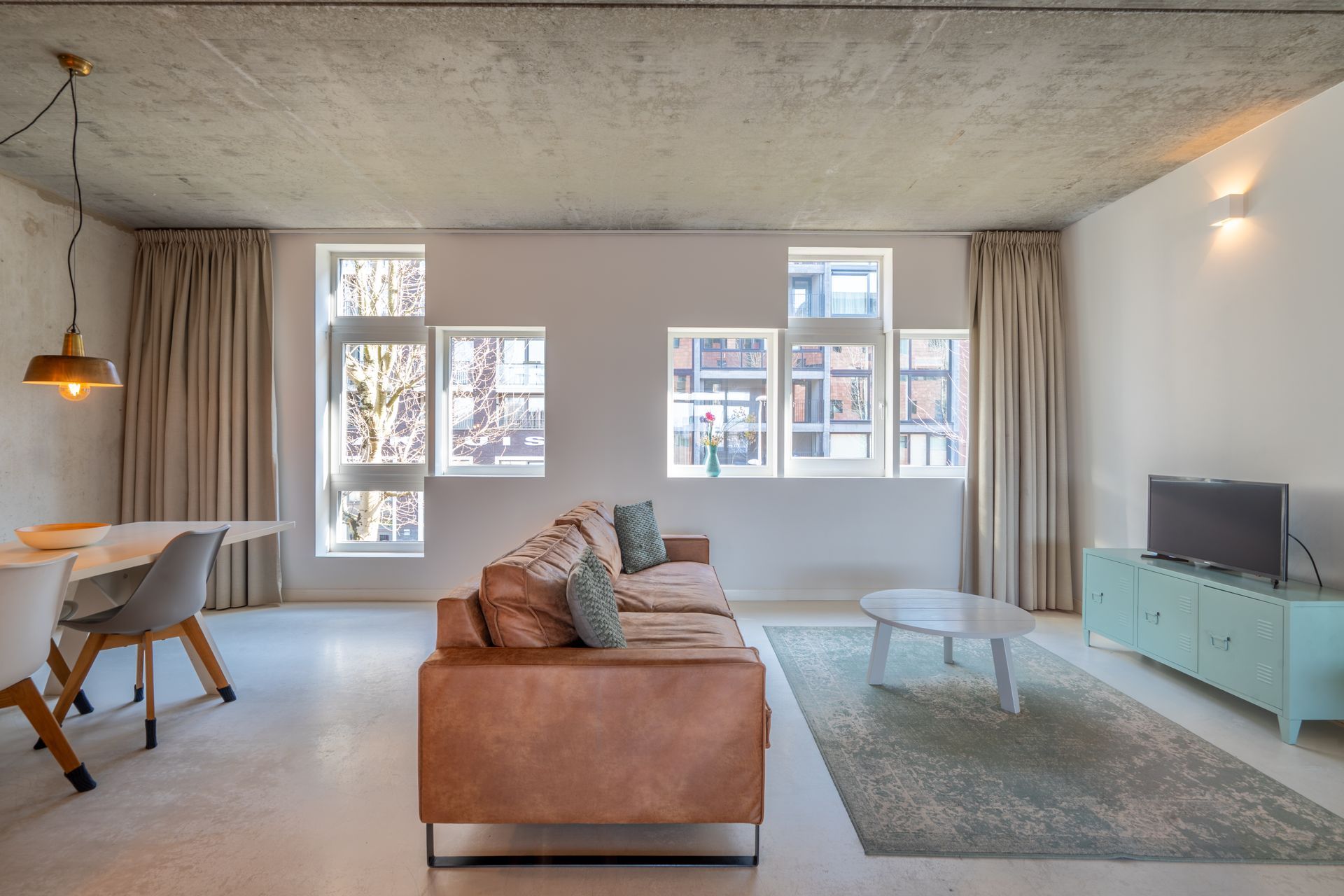 Een minimalistische woonkamer met een bruine leren bank, een lichtblauwe tv-kast, 