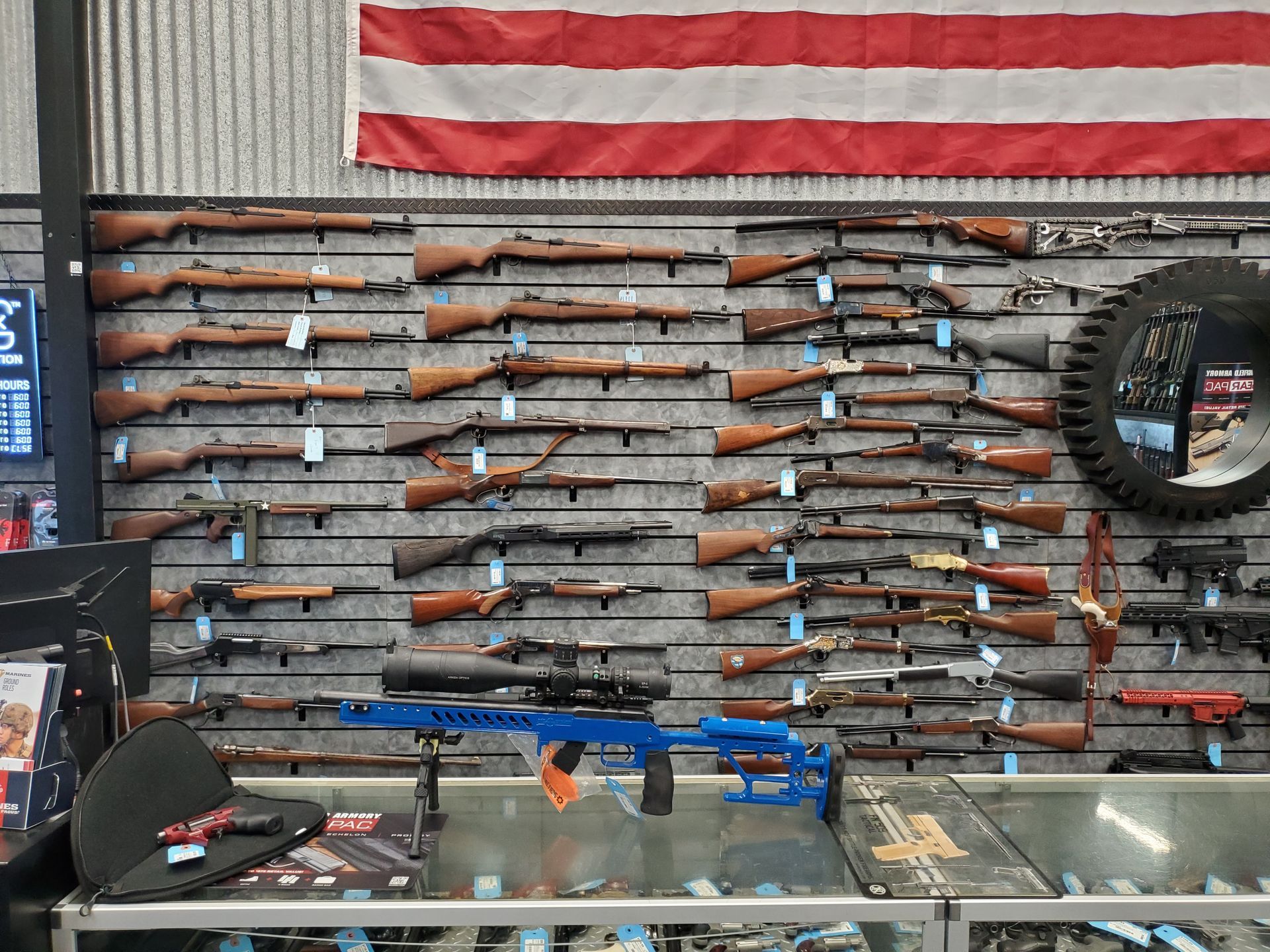 Interior of a gun store. Display racks hold rifles and shotguns, with shelving for accessories. Door on right.