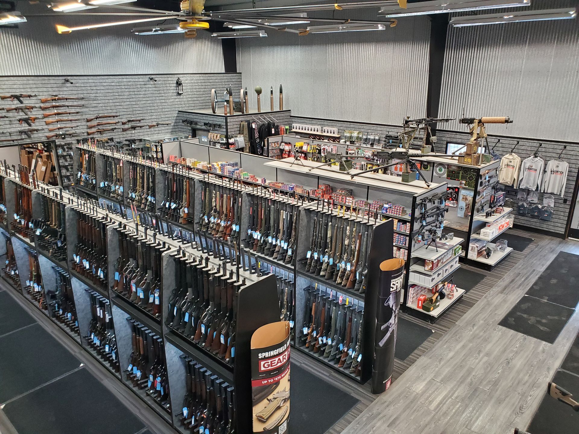 Interior of a gun store with rifles on display, shelves of ammunition, and a large ceiling fan.