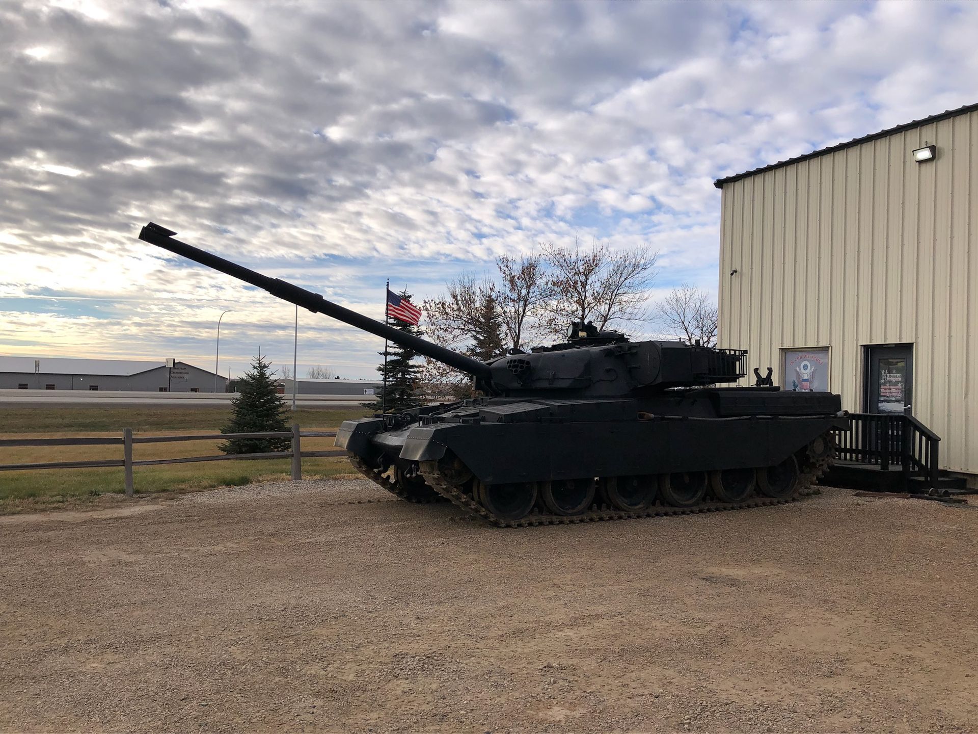 Black military tank parked on gravel next to a building, overcast sky.