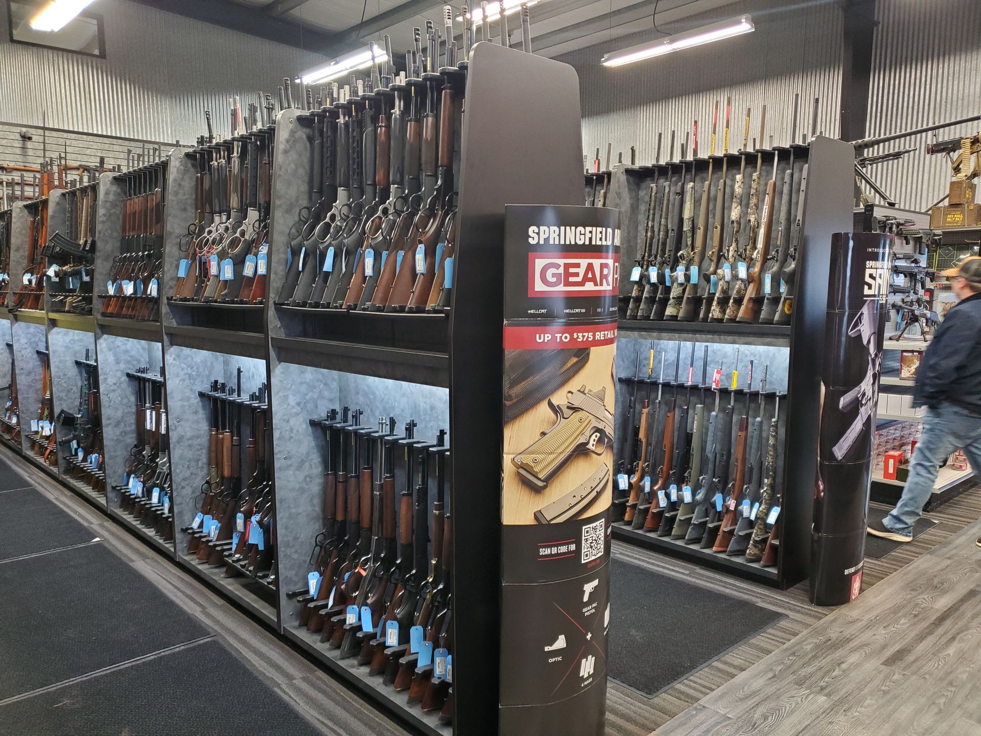 Inside a gun store, rifles and shotguns are displayed on racks and a textured wall.