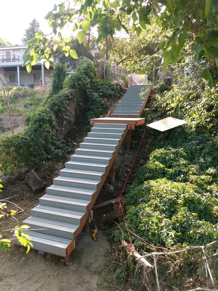 Wooden staircase built into a hillside, leading up. Green foliage surrounds the steps.