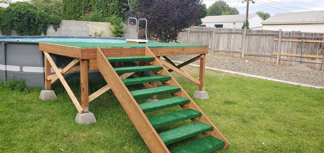 Wooden deck with stairs leading to an above-ground pool in a grassy backyard, surrounded by a fence.
