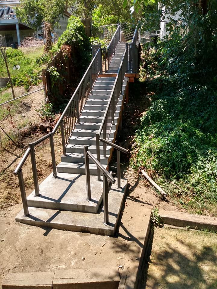 Concrete staircase with metal railings ascends a hillside.