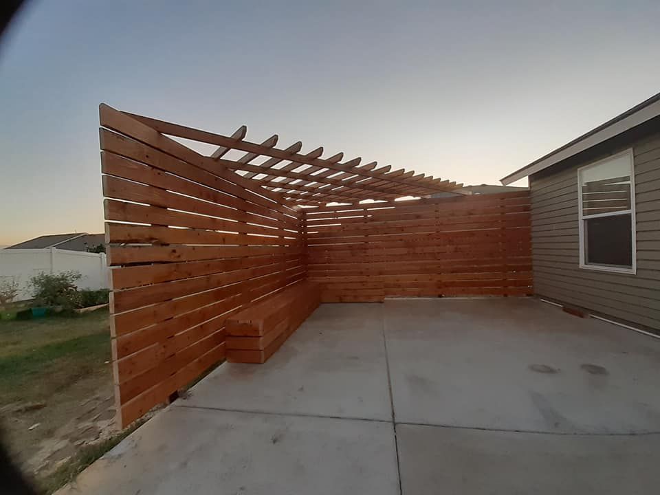 Wooden patio cover and fence attached to a house. Concrete patio.