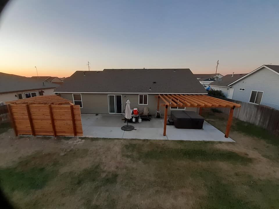 Backyard with concrete patio, pergola, hot tub, and wooden fence. House in background.