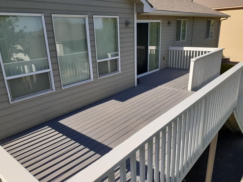 Deck with composite decking, white railings, and sliding door. Gray house exterior with multiple windows.