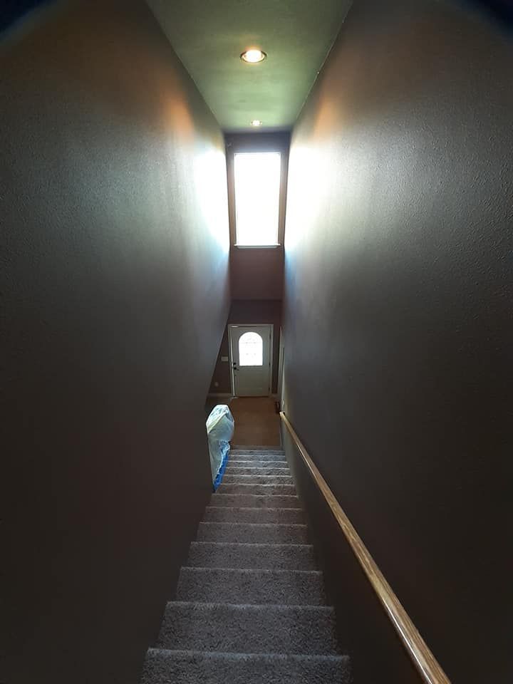 Staircase with dark walls leading up to a door at the top. A window allows light to enter the space.