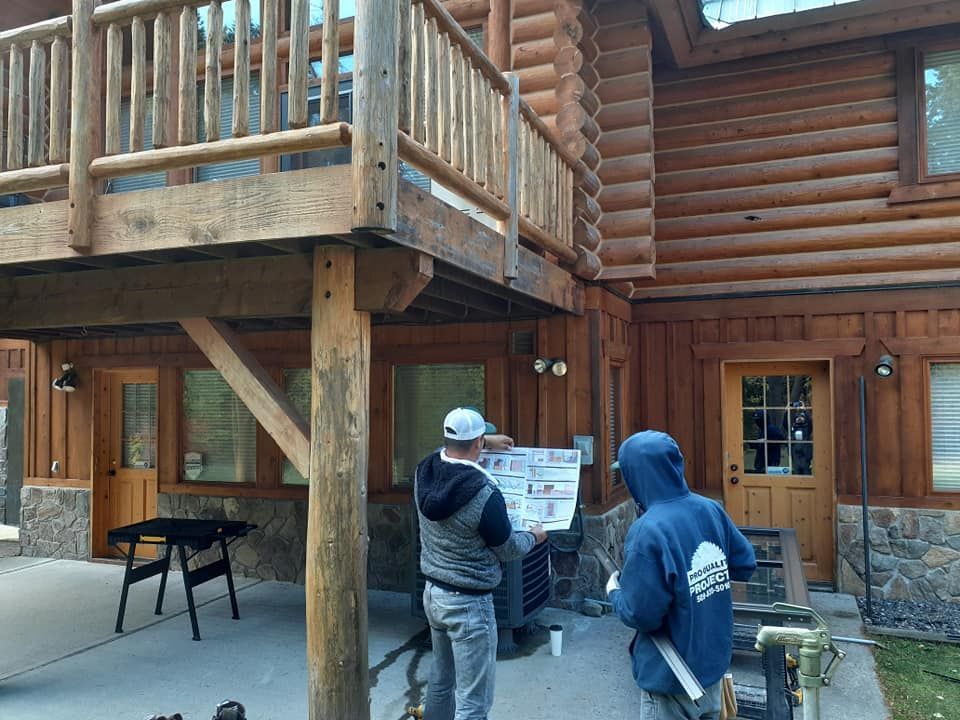 Two people looking at a chart near a log cabin's entrance, below a wooden deck.