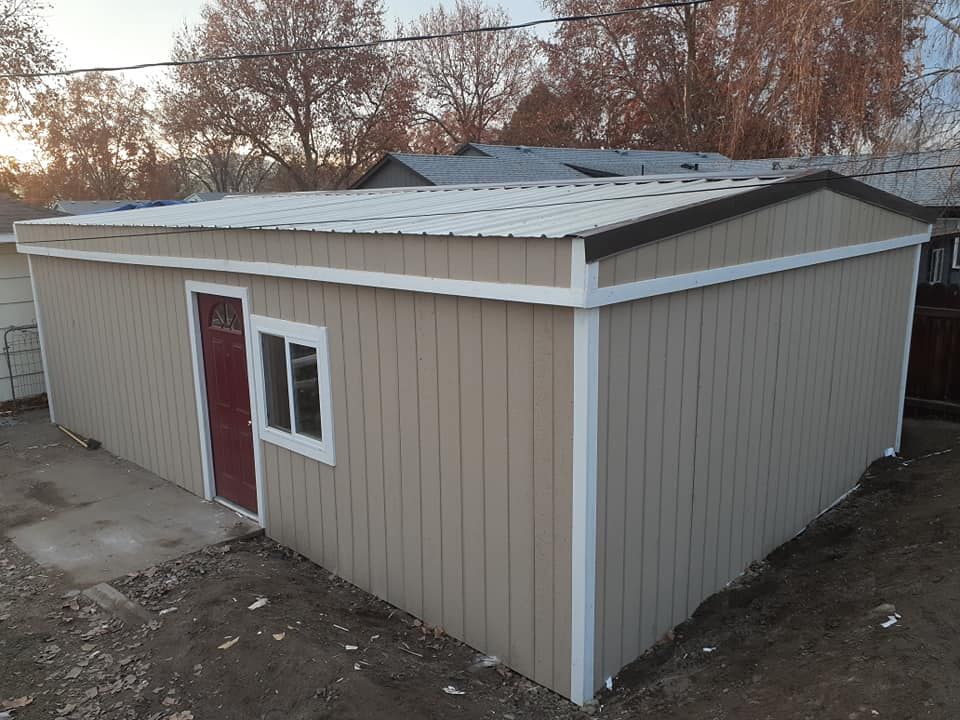 Tan rectangular building with metal roof, red door, and window.