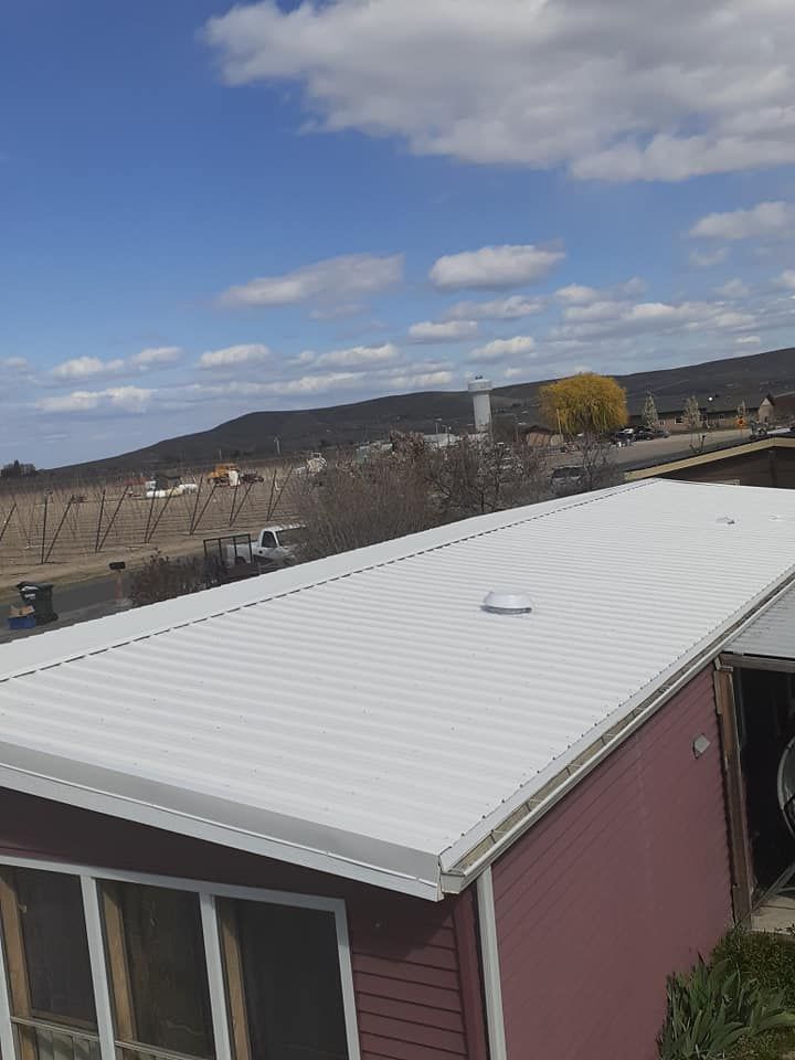 White metal roof on a red building under a partly cloudy blue sky. A distant landscape is visible.