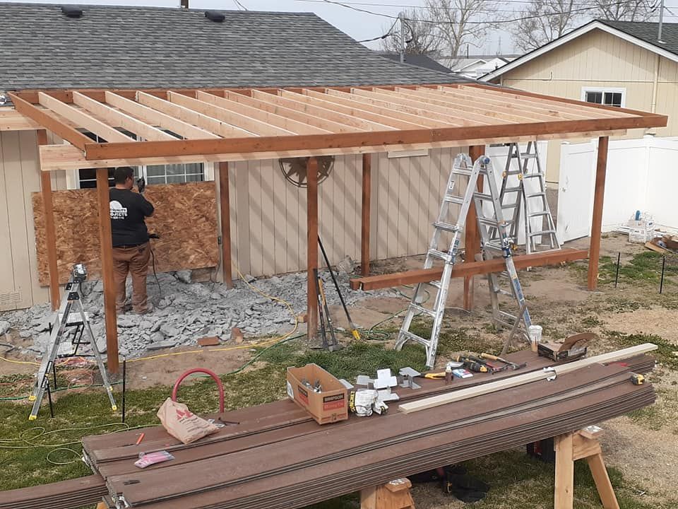 Construction of a wooden patio cover in a backyard. A person is working on the structure. Tools and materials are nearby.