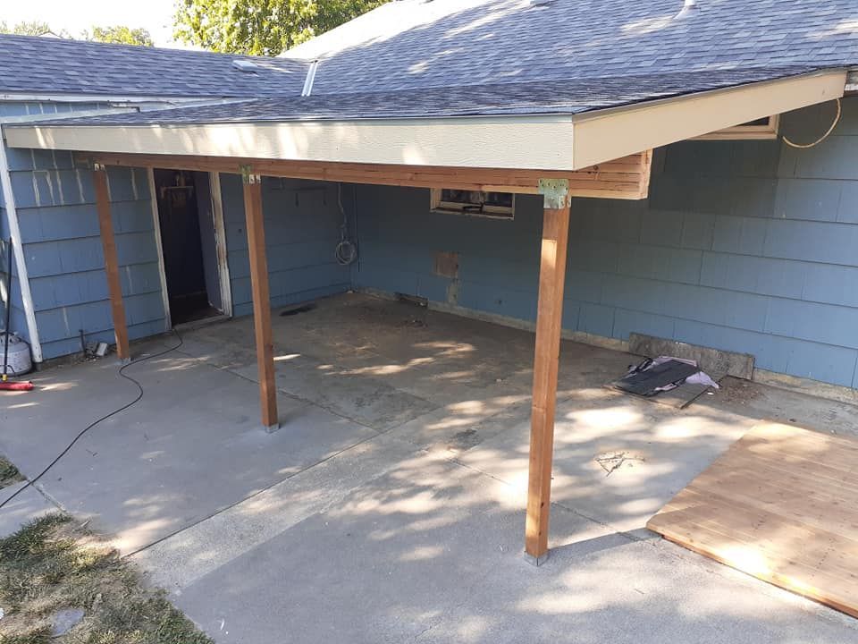 A covered patio with a concrete floor. Wooden posts support the roof.