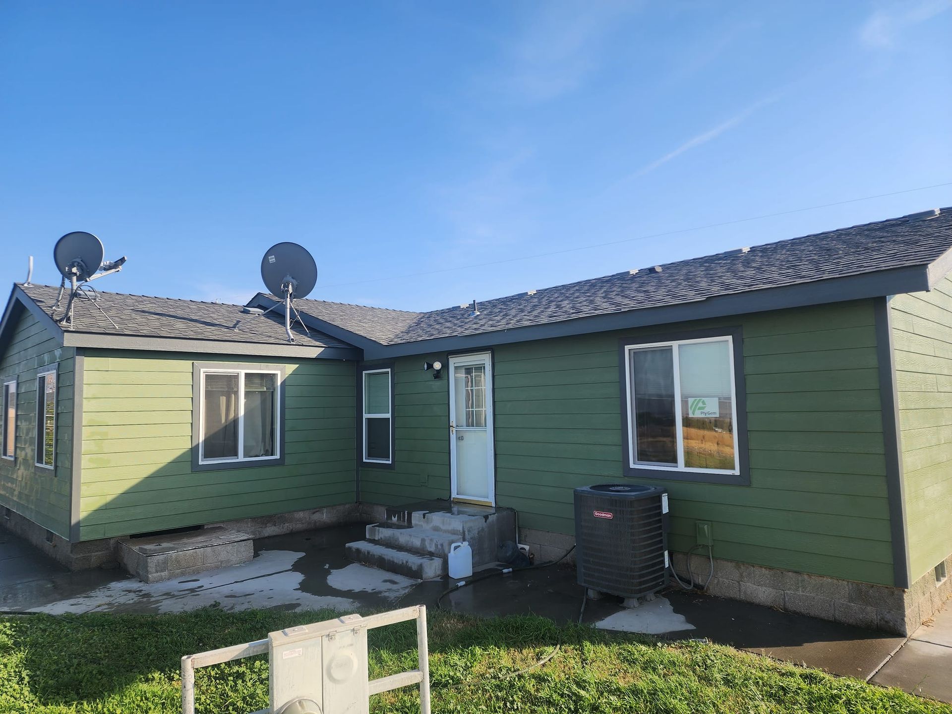 Green house with dark roof and two satellite dishes against a blue sky.