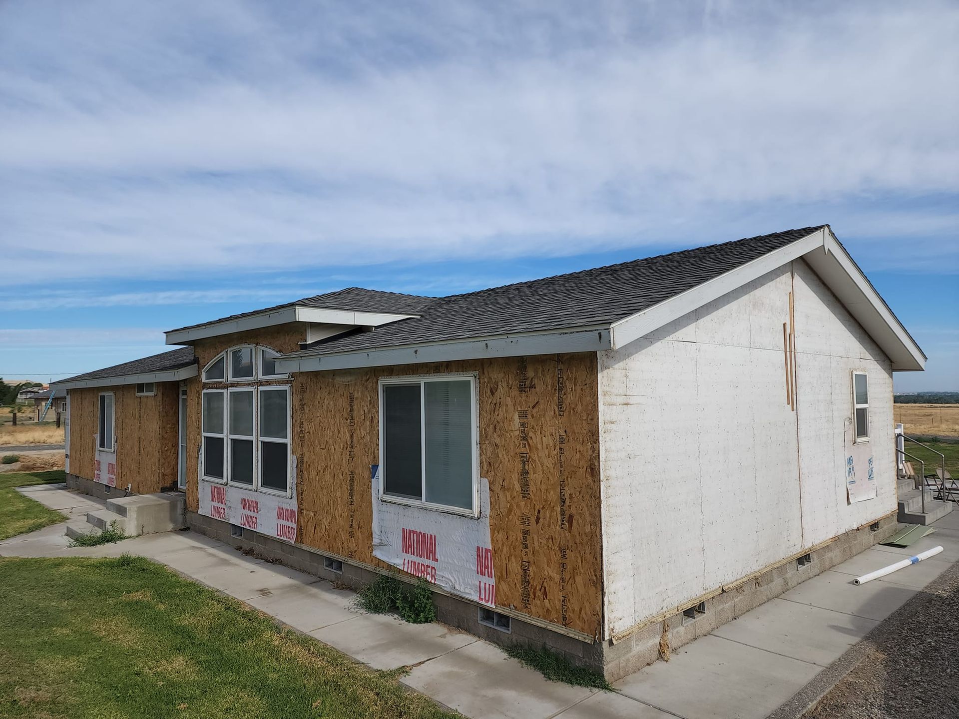 House under construction with exposed wooden frame and sheathing, blue sky.
