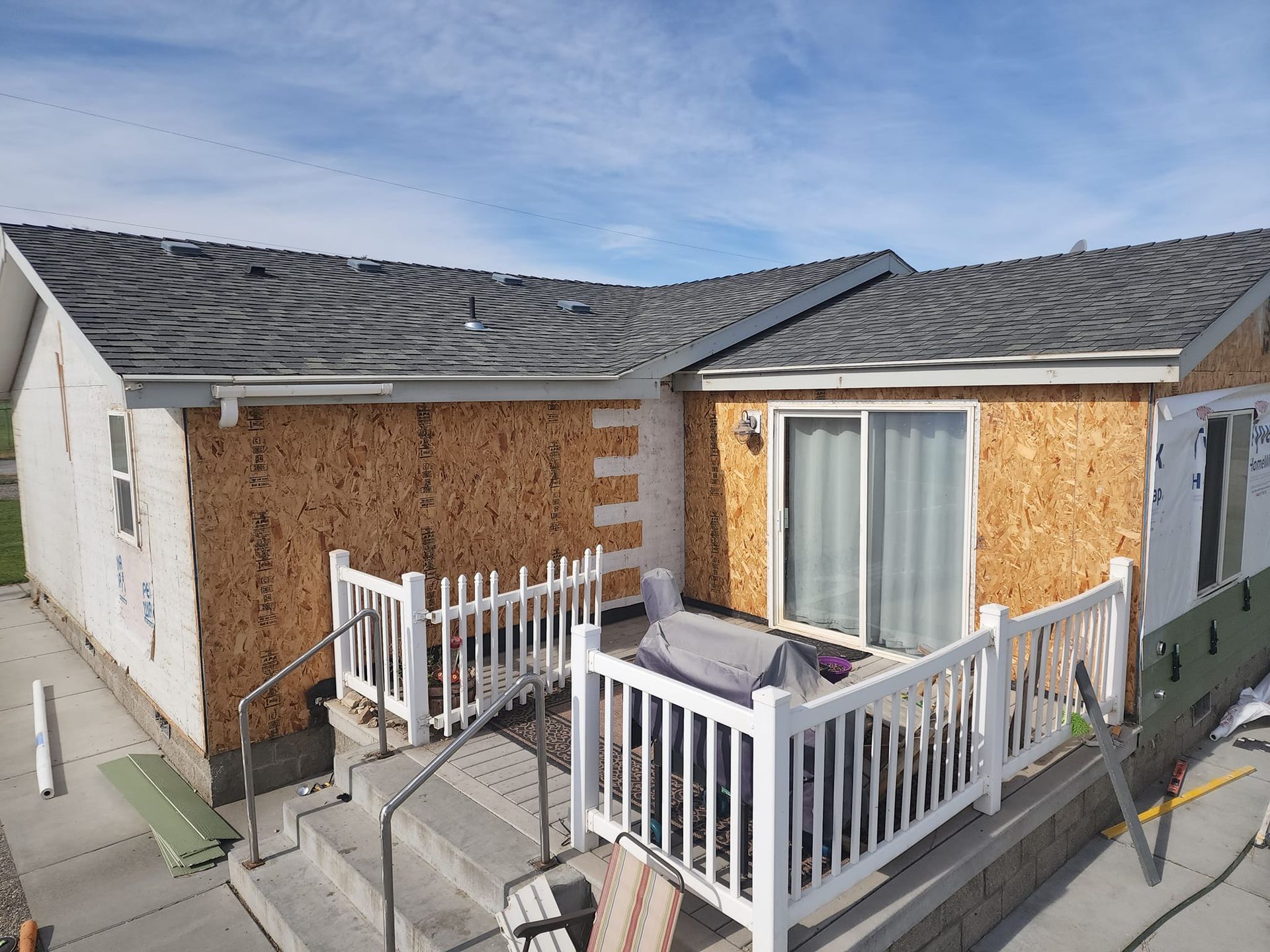 House exterior under construction, with exposed OSB sheathing. White railing and sliding glass door visible.