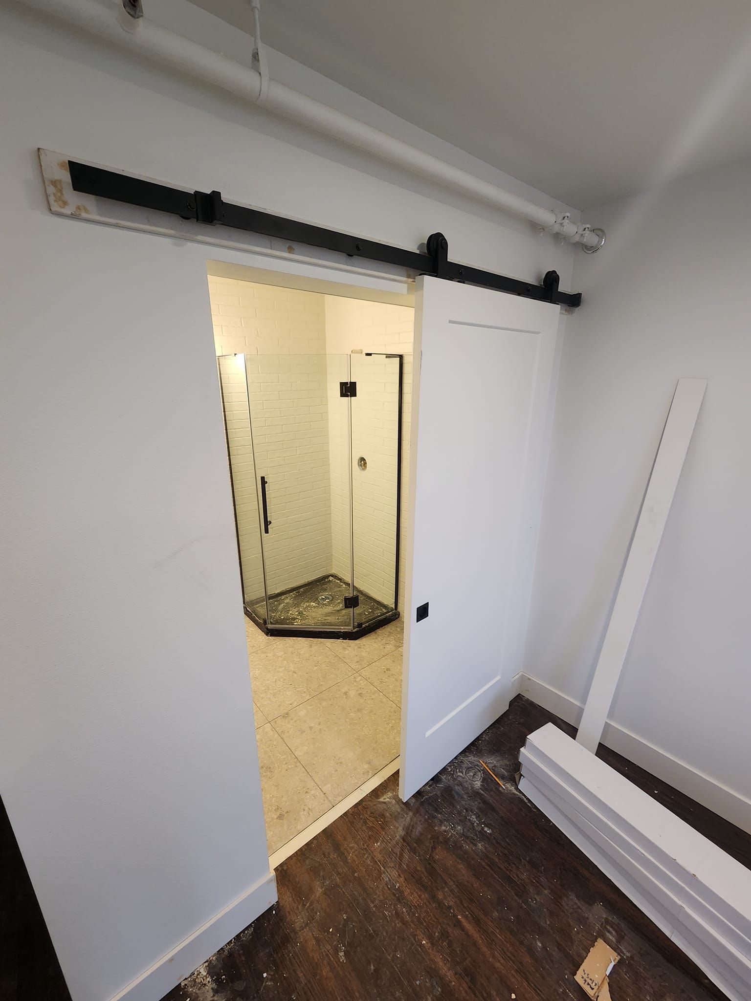 White barn door partially open revealing a bathroom with a shower. Black door hardware and white walls.