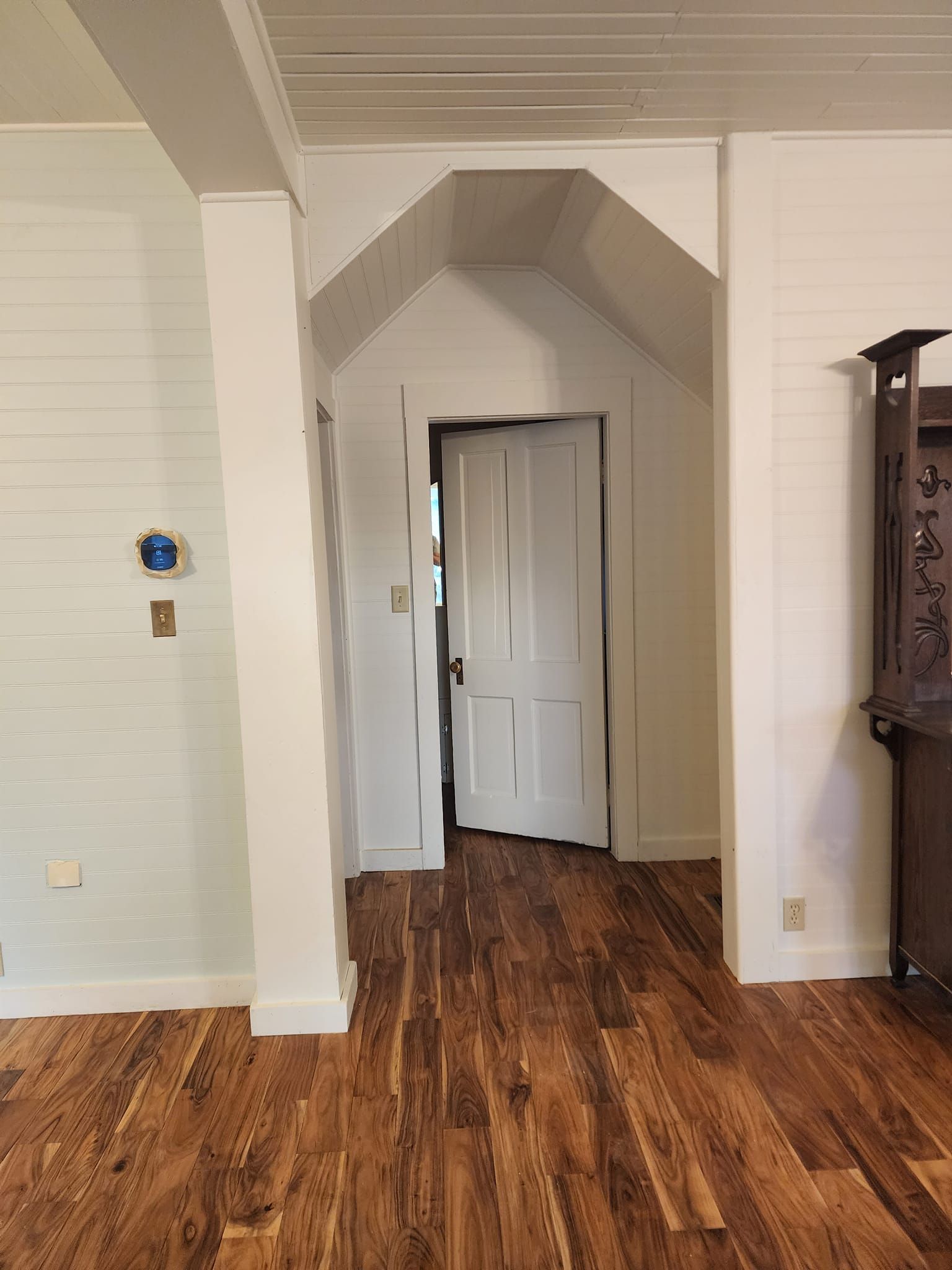 White-painted interior with wood floors and a door. A post and white wall are on the left; a cabinet is on the right.
