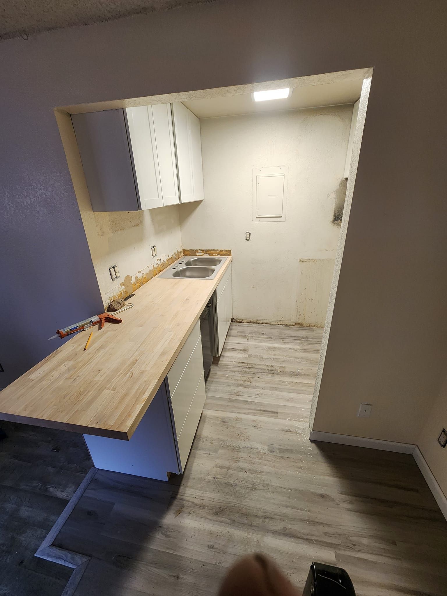 A kitchen with cabinets, a counter, and sink under construction. Light wood countertop, neutral colors.