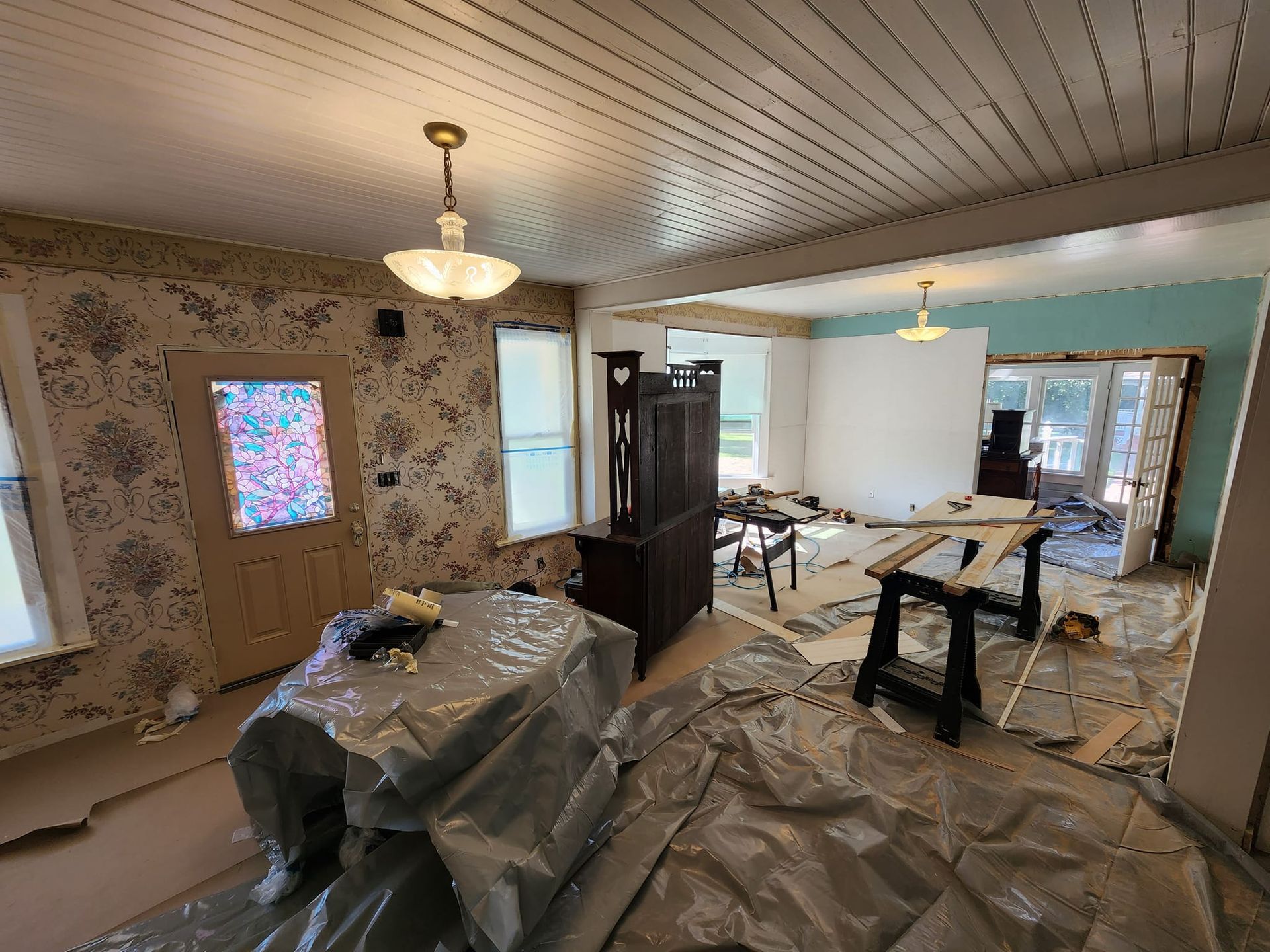 Room under renovation with furniture covered, open doorway to another room with turquoise wall.
