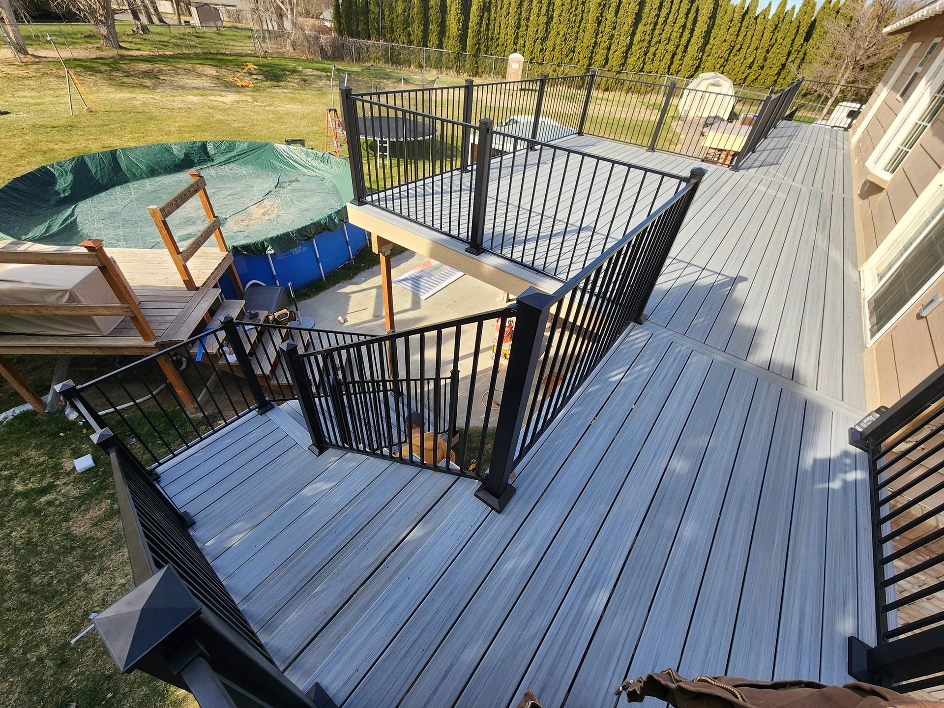 High-angle view of a gray composite deck with black railings, stairs leading to a backyard pool.