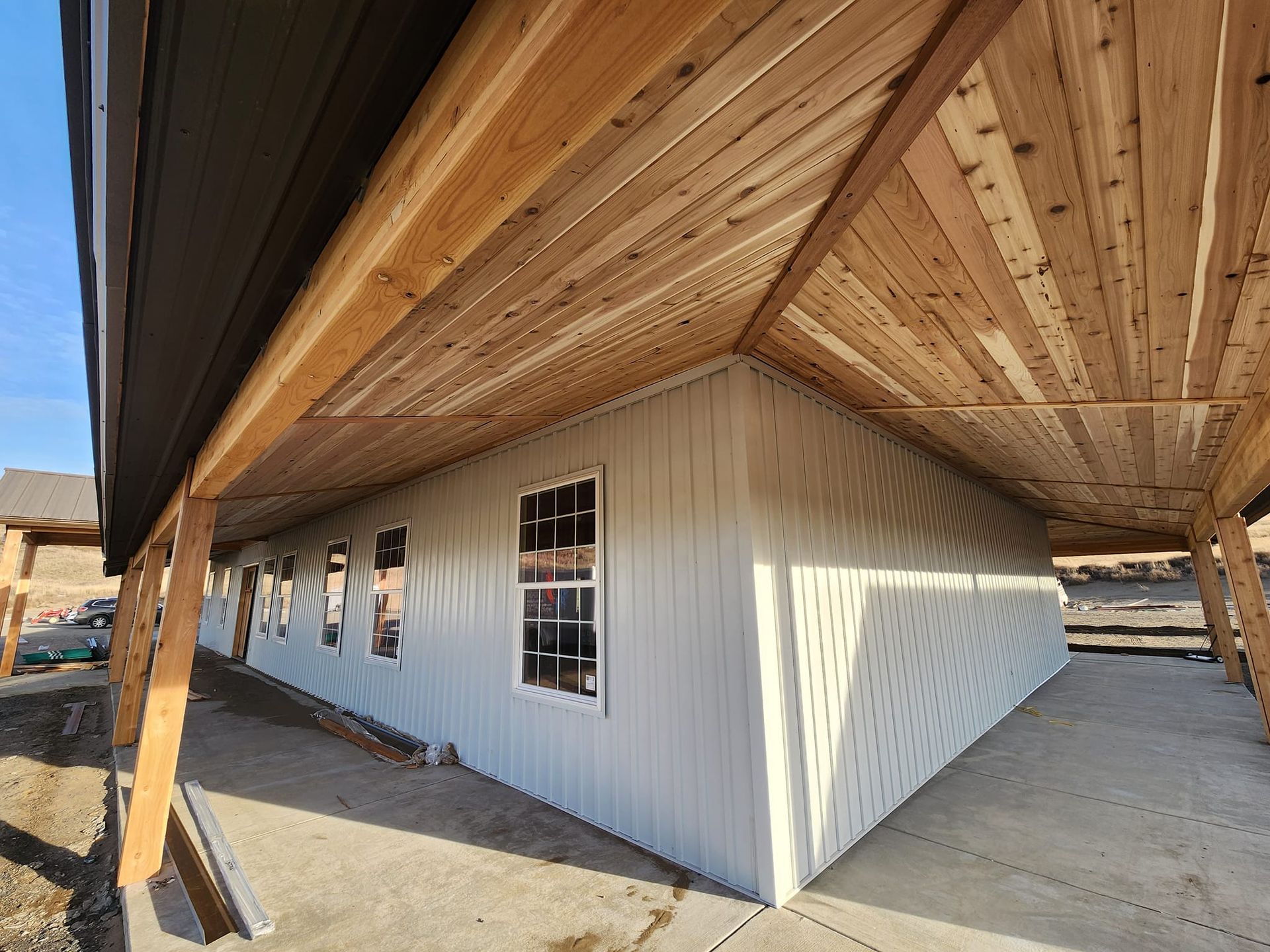 Exterior of a building under construction. White siding, wooden ceiling, and dark roof.