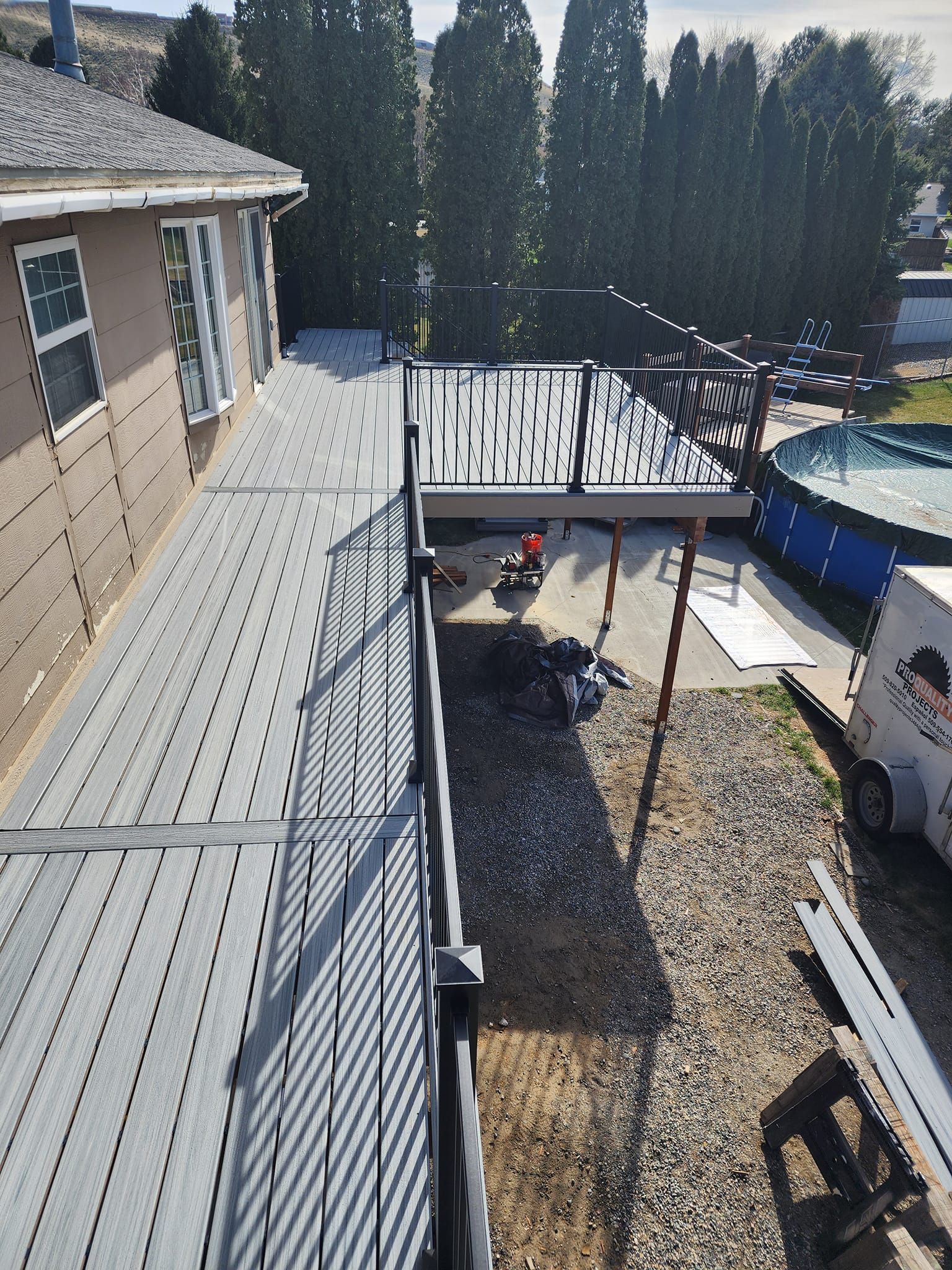 View of a deck under construction with gray composite decking, black railing, and a pool in the background.