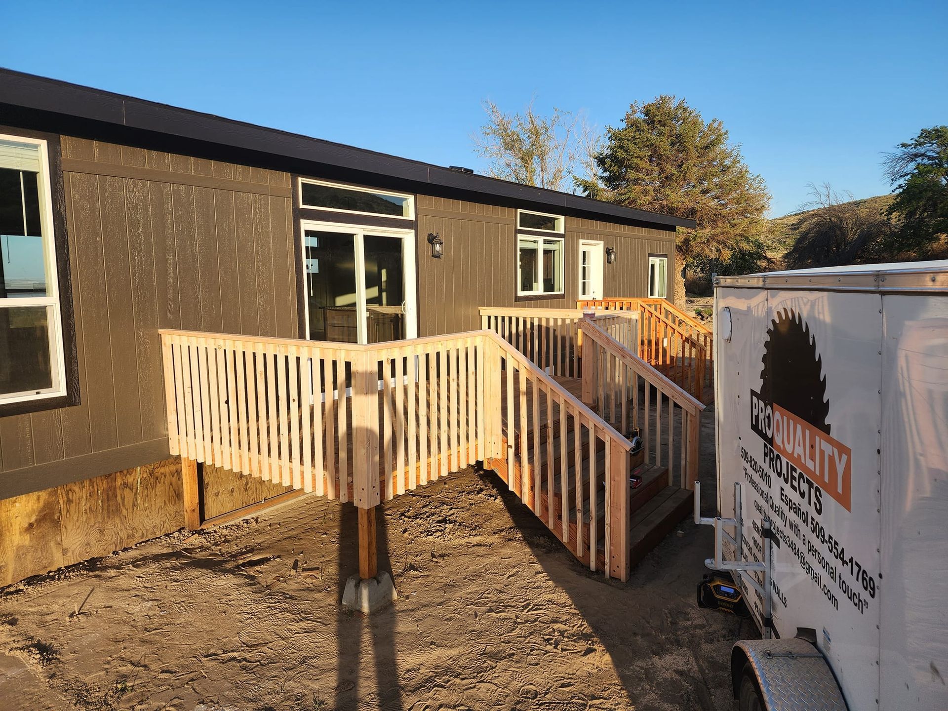 Exterior view of a dark-colored building with a wooden deck and stairs. A trailer with a logo is to the right.