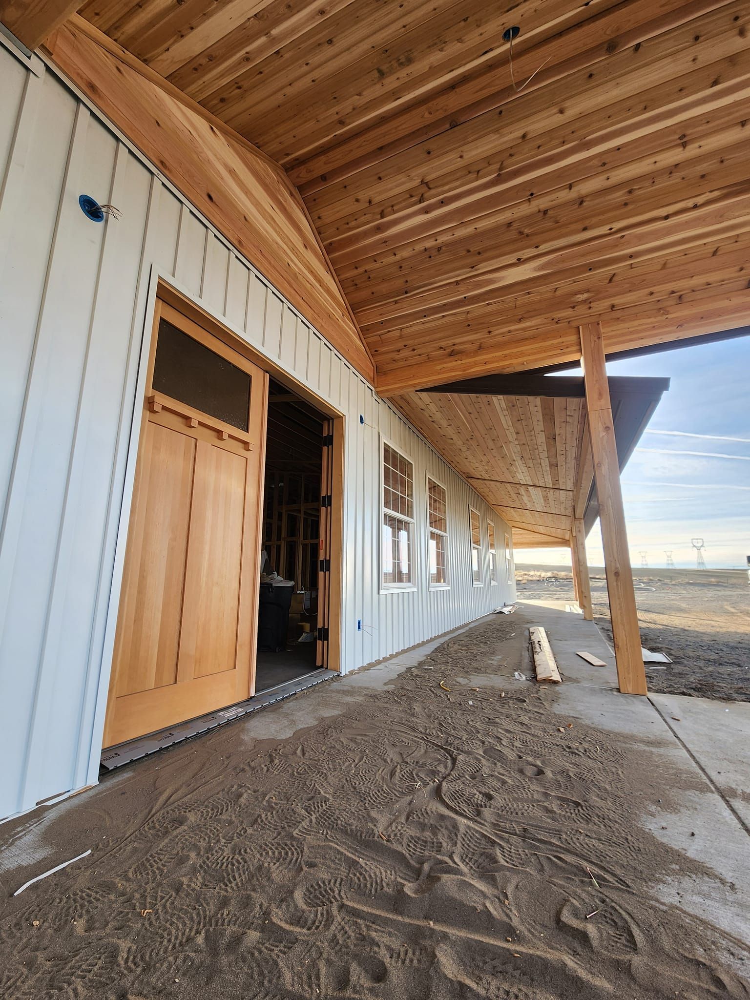 Exterior of a building with white siding, wooden door and porch, and dirt ground.