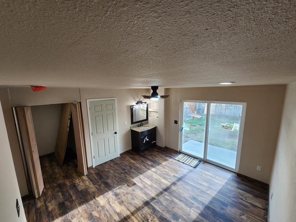 Empty room with wood floors, sliding glass door to yard, door to the left, and a vanity.