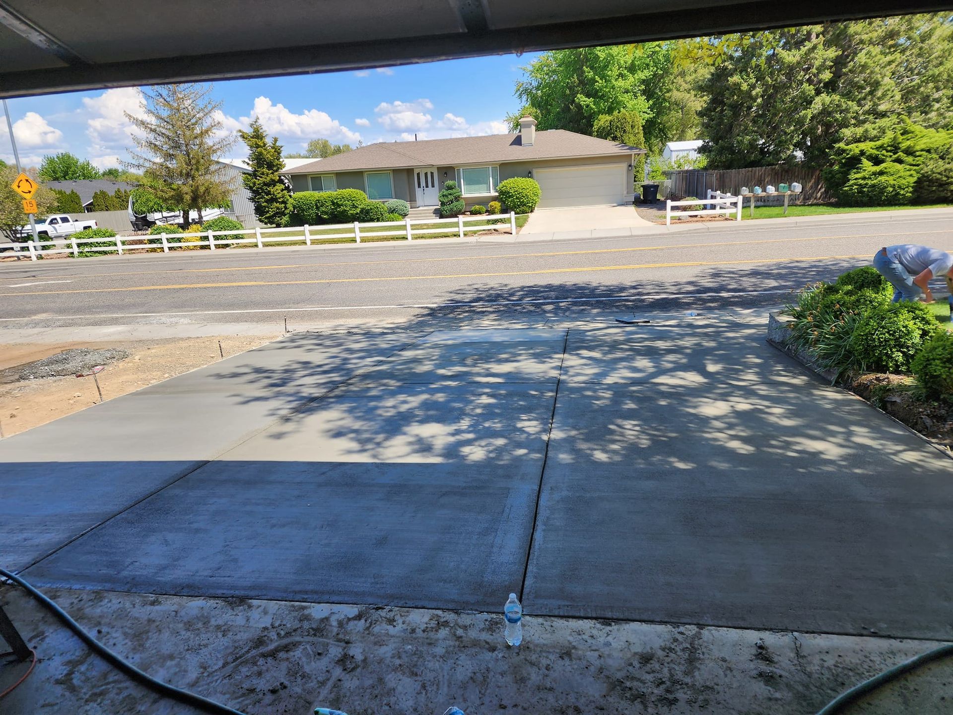 Newly poured concrete driveway with a house in the background. A person is near some bushes on the right.