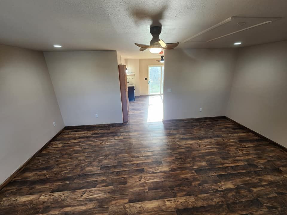 Empty room with dark wood-look floor, light walls, and a ceiling fan. Bright light streams from doorway.