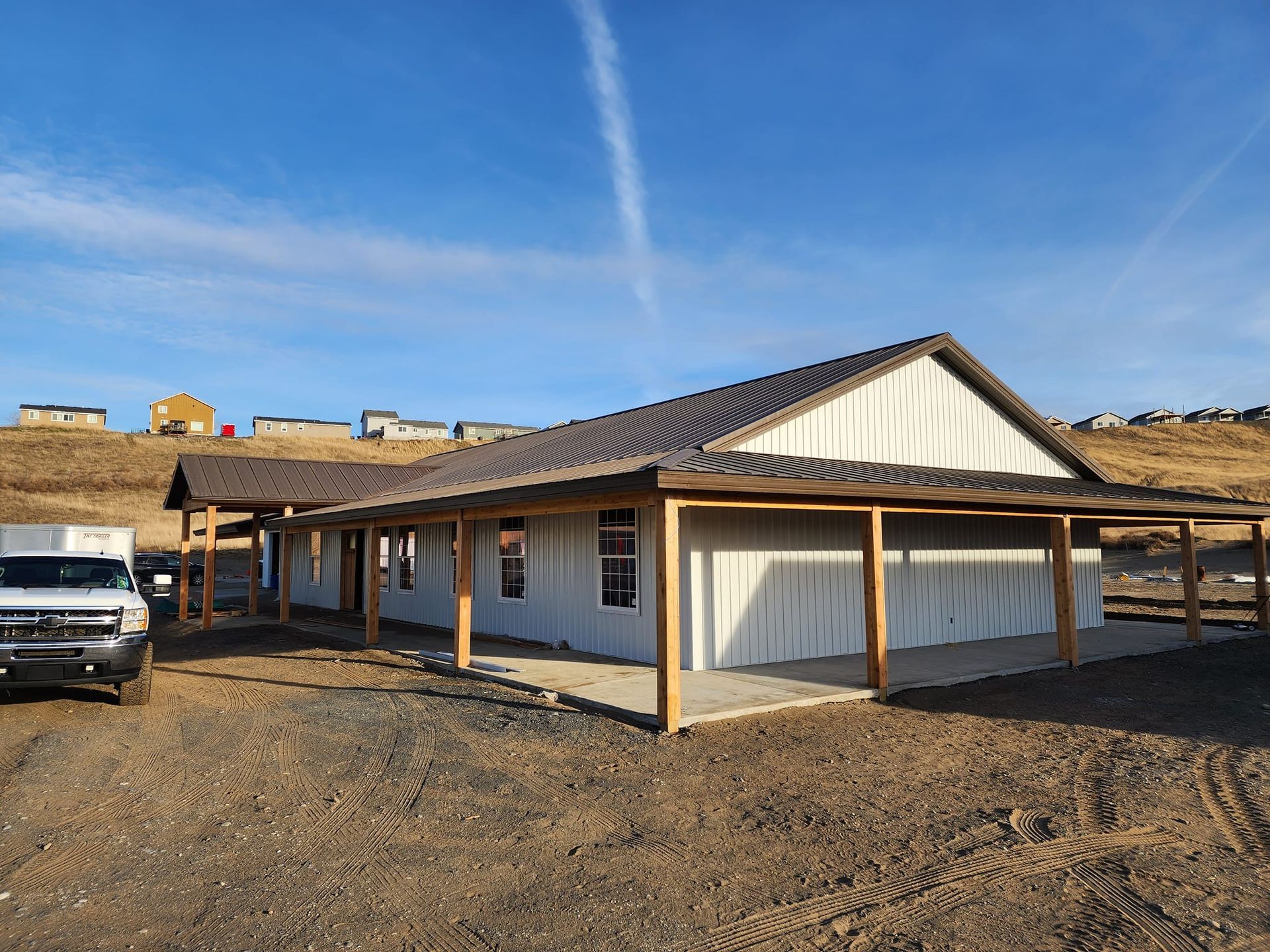 A one-story building with a covered porch and metal roof under a blue sky, on a dirt lot.