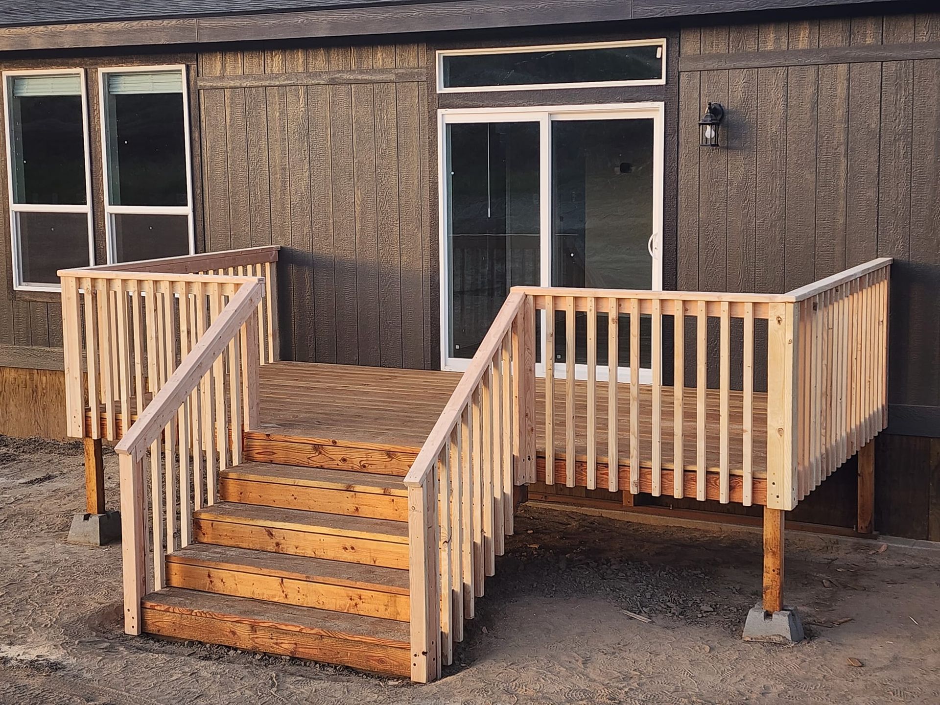 Wooden deck with stairs leading to a sliding glass door; deck has railing and is attached to a gray building.