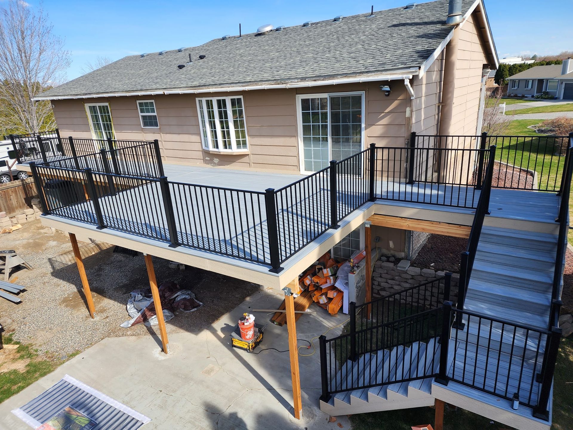 Elevated wooden deck with black railings and stairs attached to a tan house.
