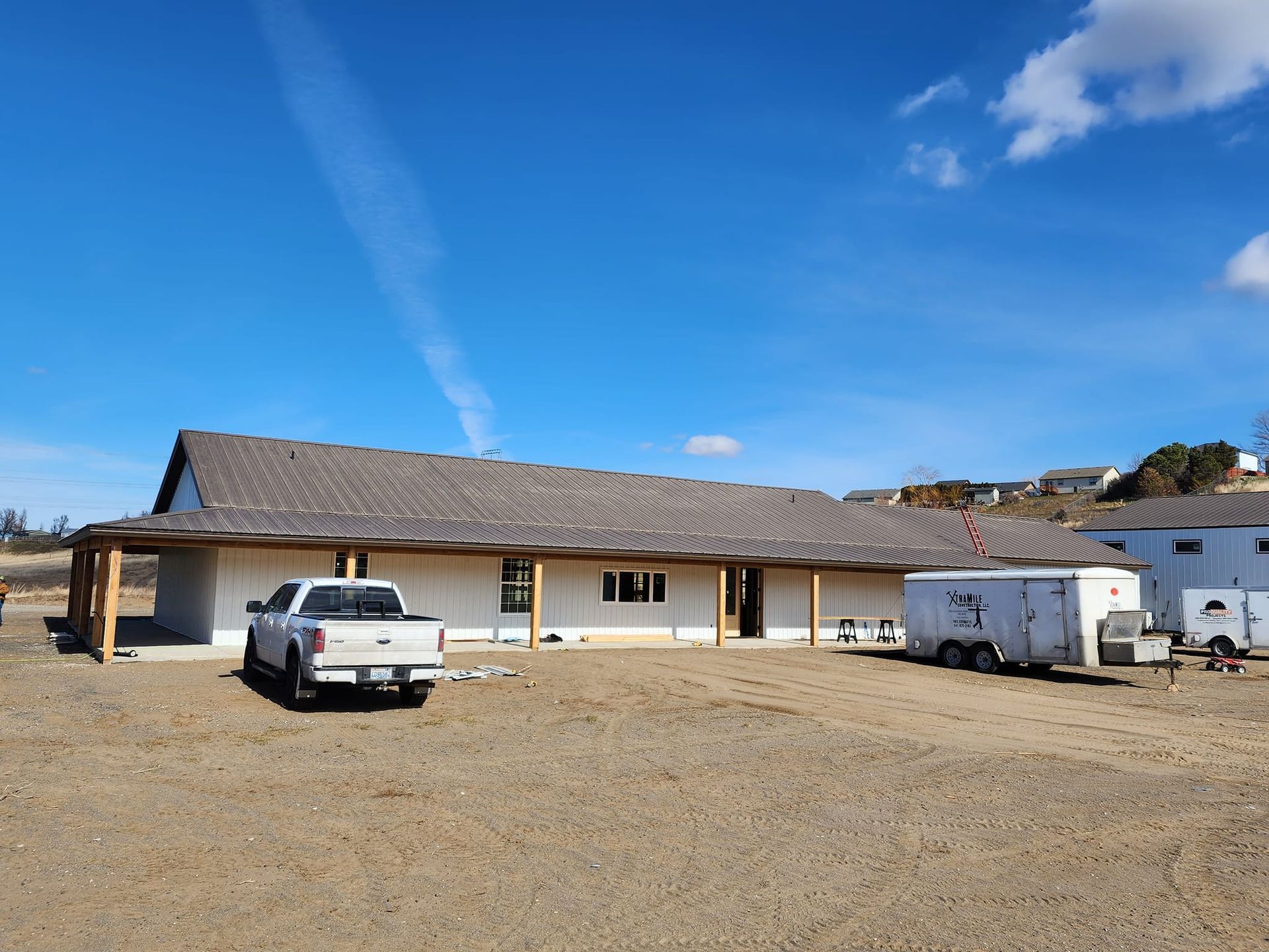 A long, single-story building under construction with a pickup truck and trailer parked outside on a gravel lot.
