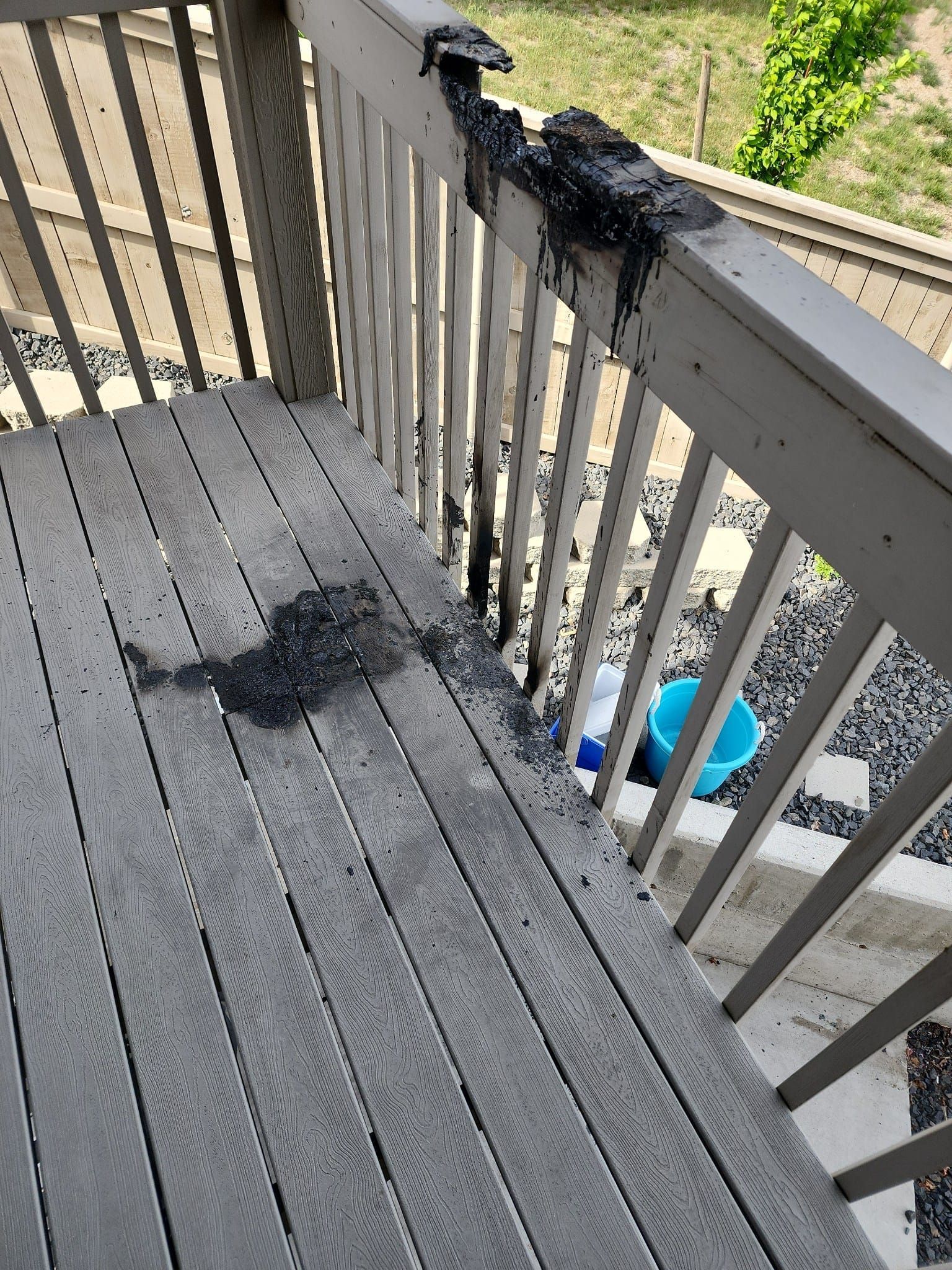 Damaged gray deck with charred railing and debris. A blue bucket is visible.