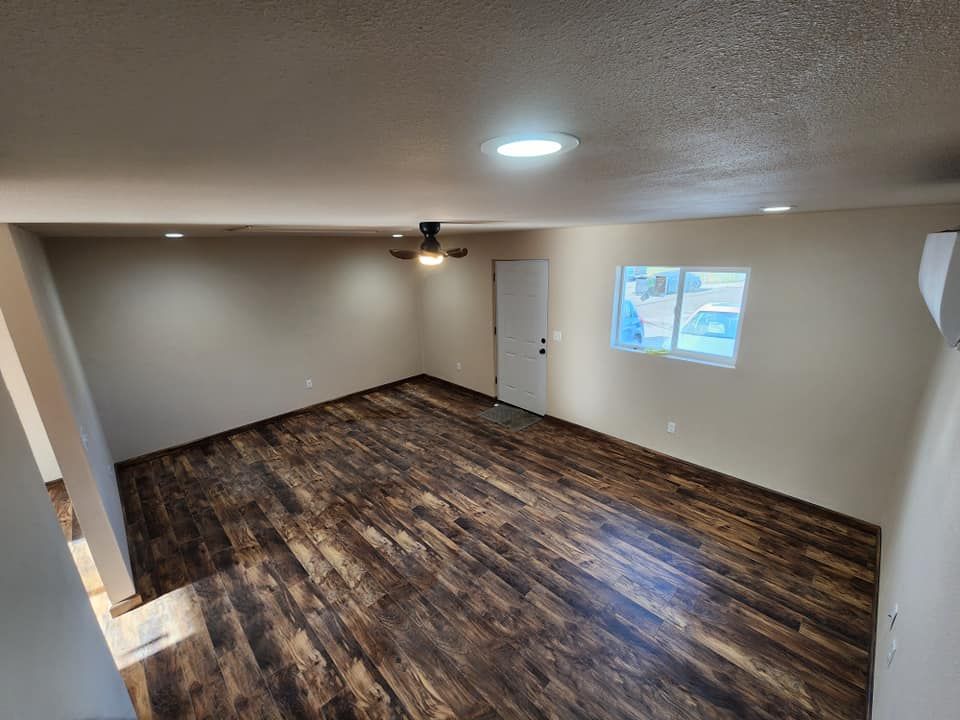 Empty room with dark wood-look flooring, beige walls, recessed lights, a door, and a window.