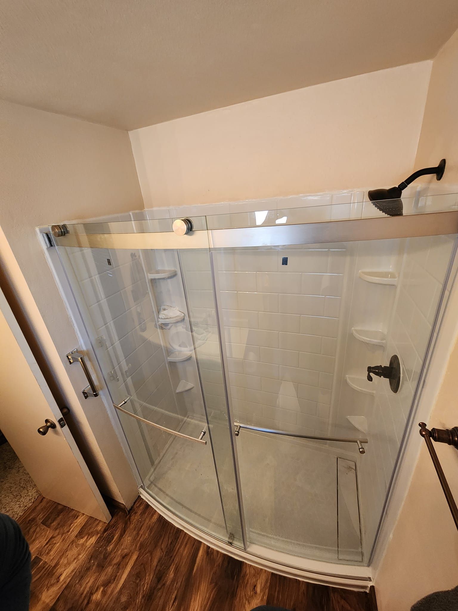Curved glass shower enclosure with sliding doors and dark fixtures, situated in a bathroom.
